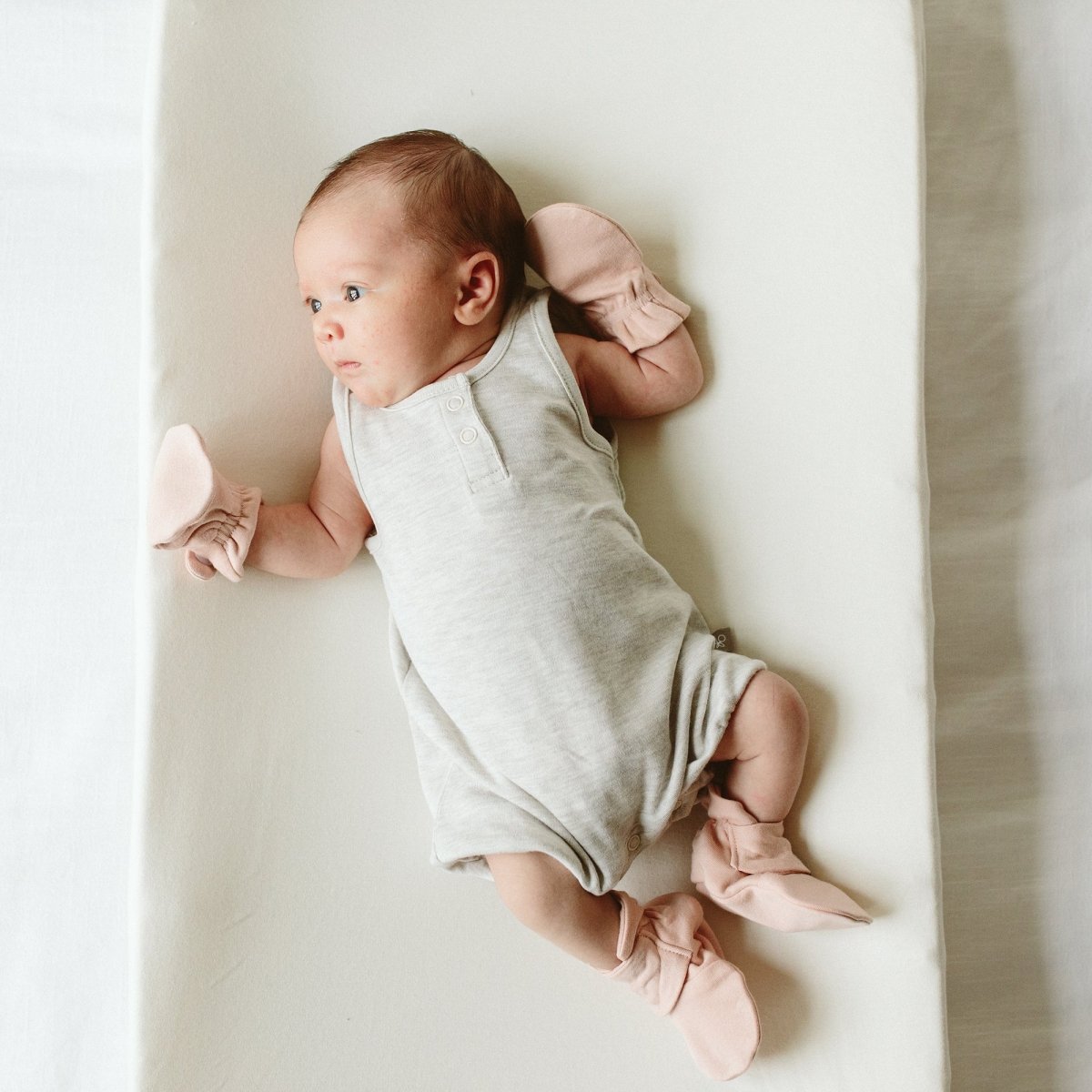 Newborn baby in a light gray outfit with pink bows on a white background