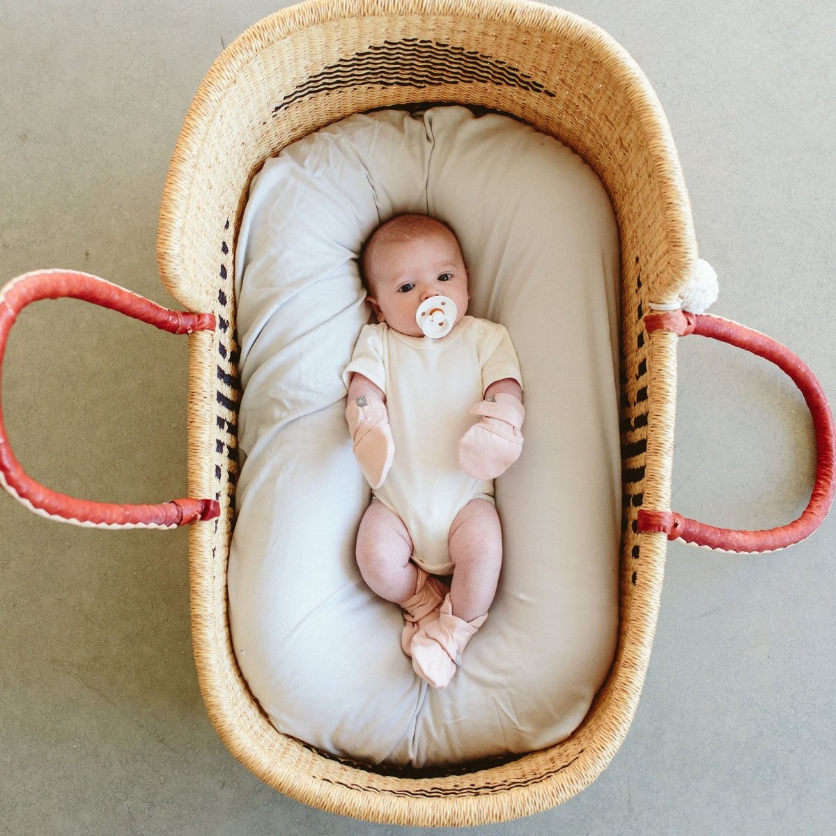 Newborn baby in a wicker crib with a pacifier on a neutral background