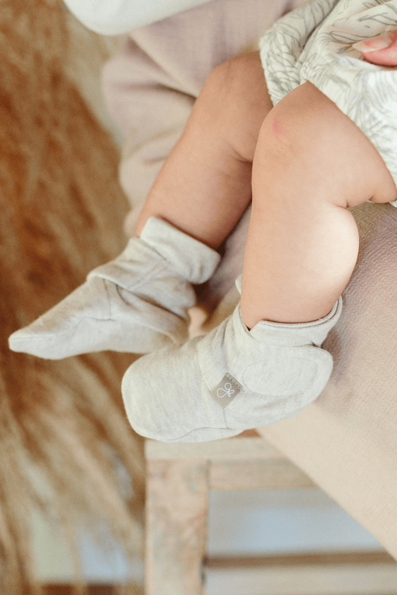 Baby's legs wearing light gray booties on a blurred background