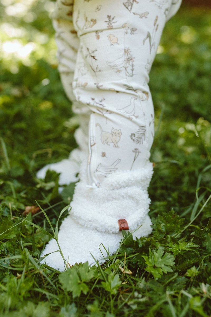 A child's legs wearing patterned leggings with white fuzzy booties on a grassy background
