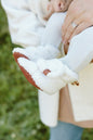 Close-up of a person holding a white baby bootie with a blurred green background