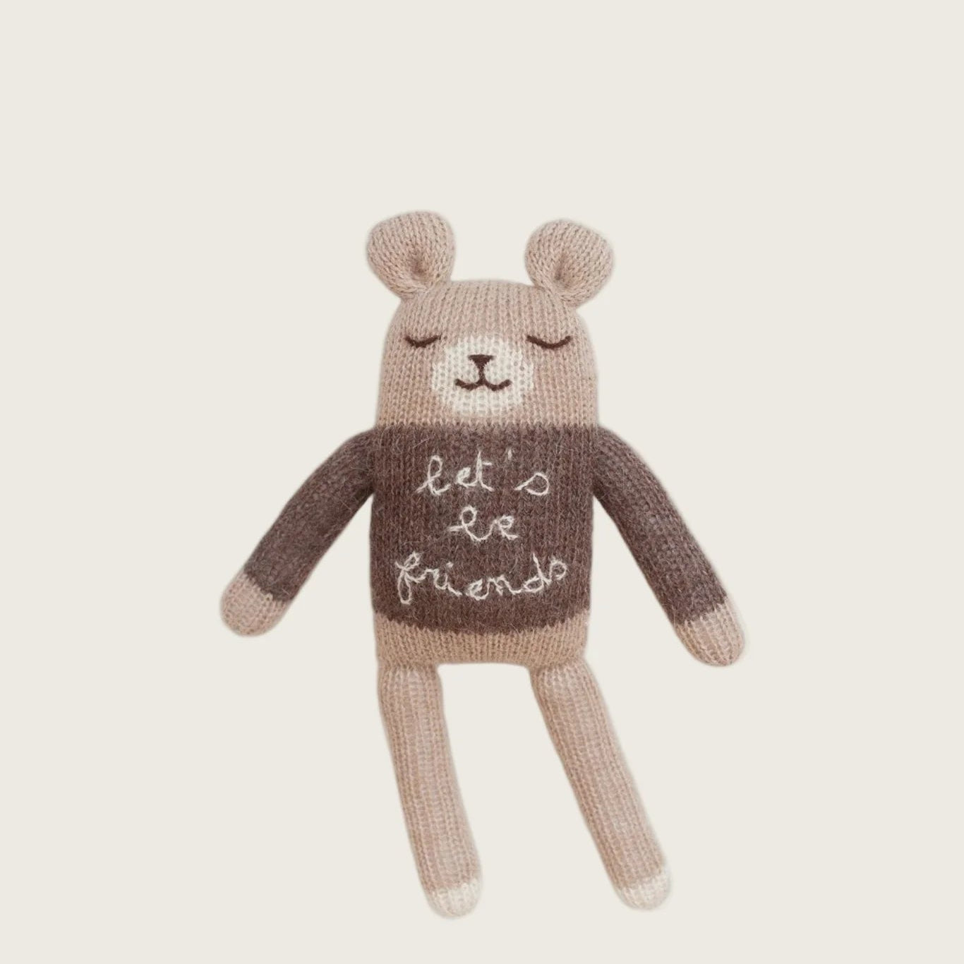 Knitted teddy bear wearing a sweater with 'let's be friends' text on a beige background