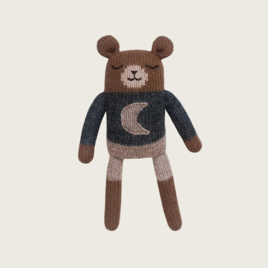 Knitted teddy bear wearing a sweater with a moon design on a beige background