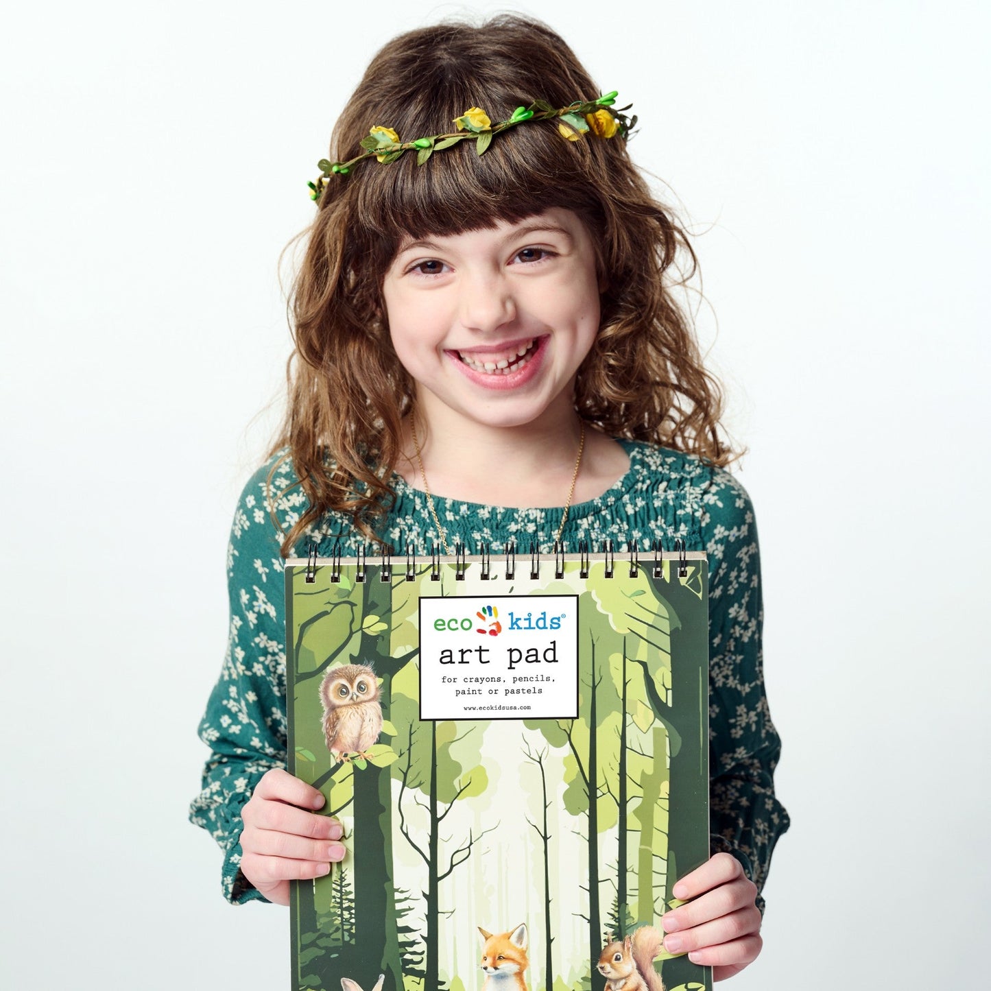 Girl holding an eco kids' art pad with a forest design on a white background