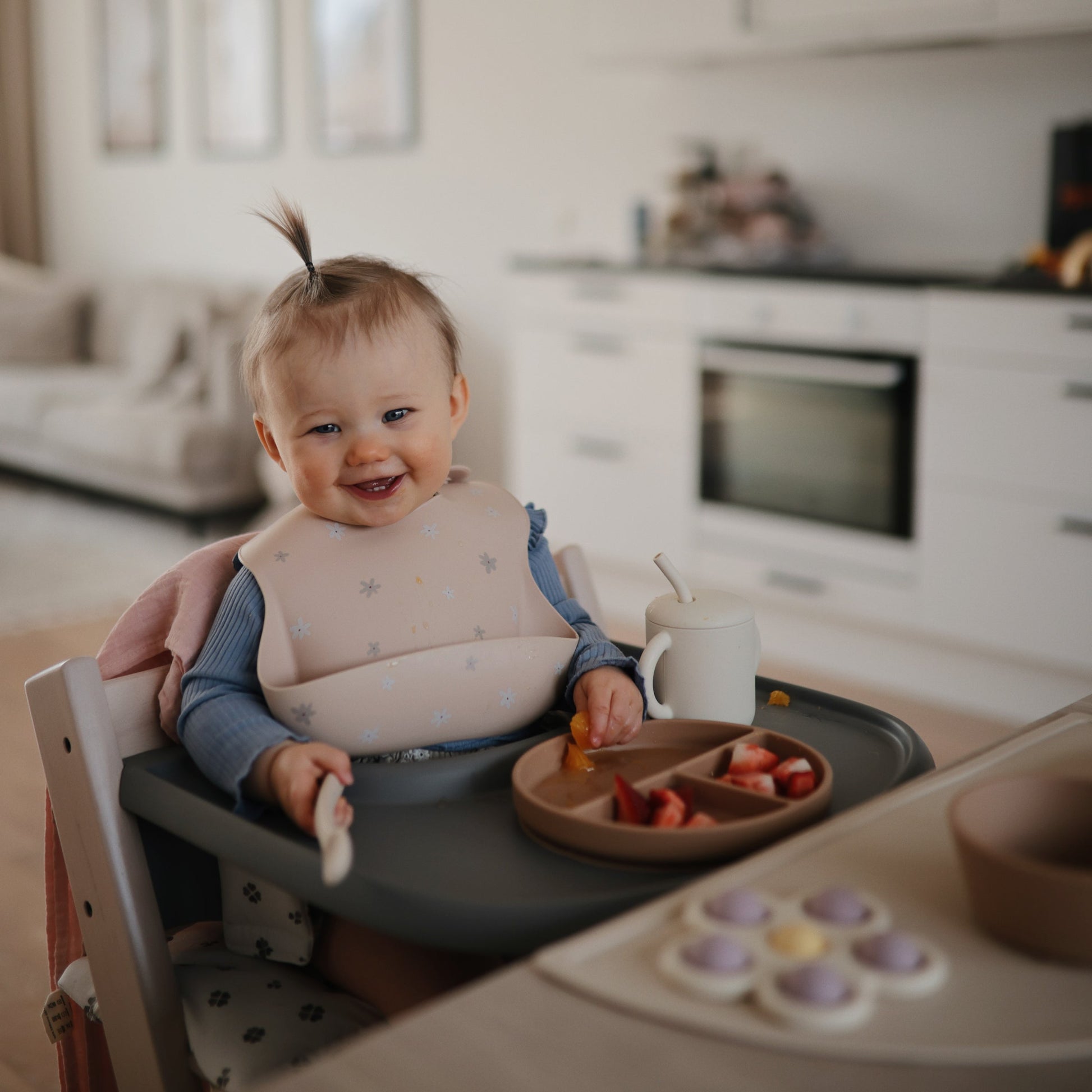 Baby sitting in a high chair with a plate of food in a kitchen setting