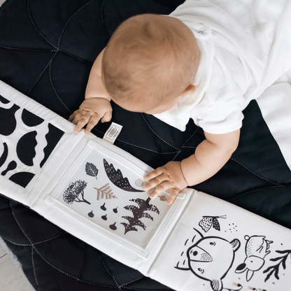 Baby interacting with a book featuring black cut-out designs on a dark surface