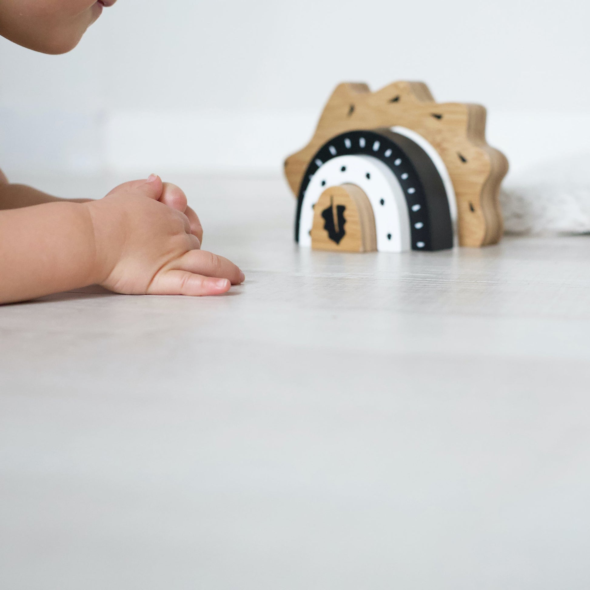 Child's hand reaching towards a wooden toy with black and white design on a white surface.