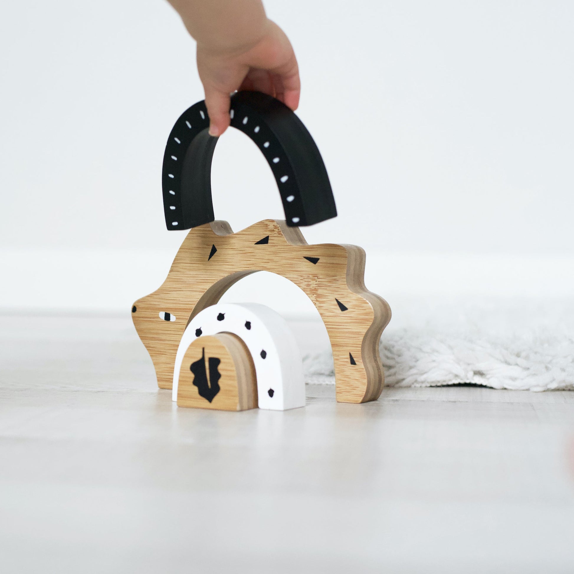 Wooden toy arch with black cutouts held by a hand on a white background