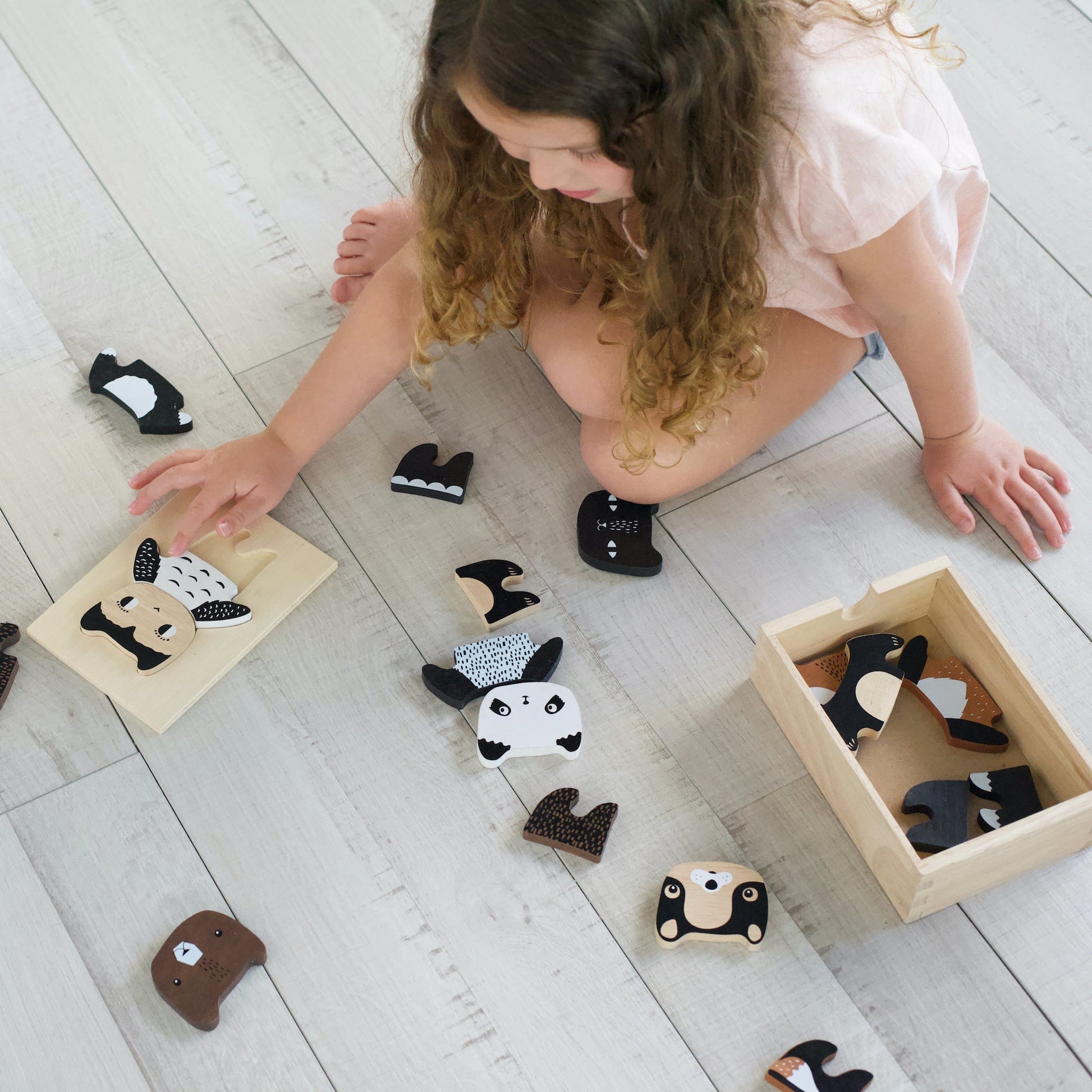 Child playing with wooden animal toys on a light wooden floor