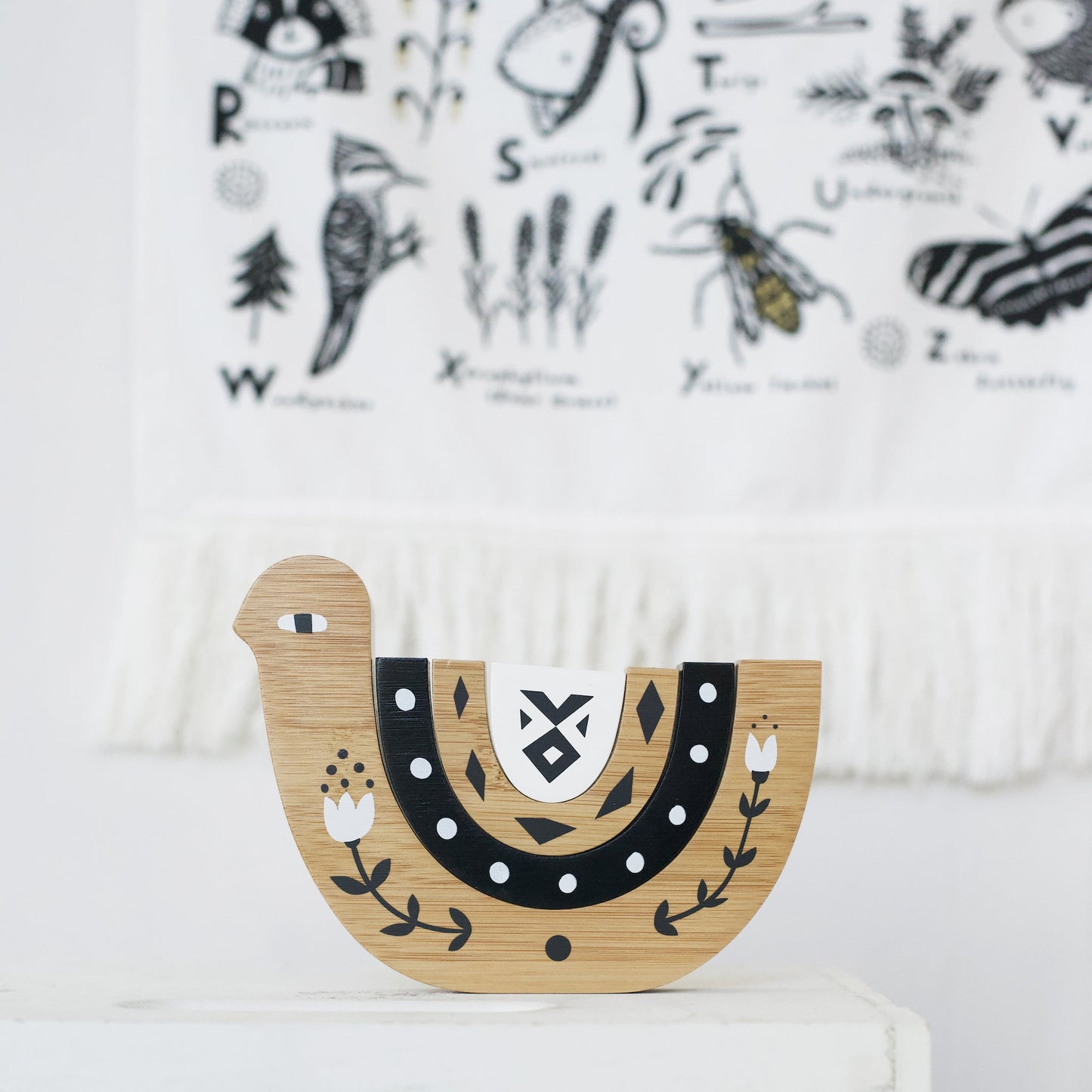 Wooden toy shaped like a bird with black and white patterns on a white surface.