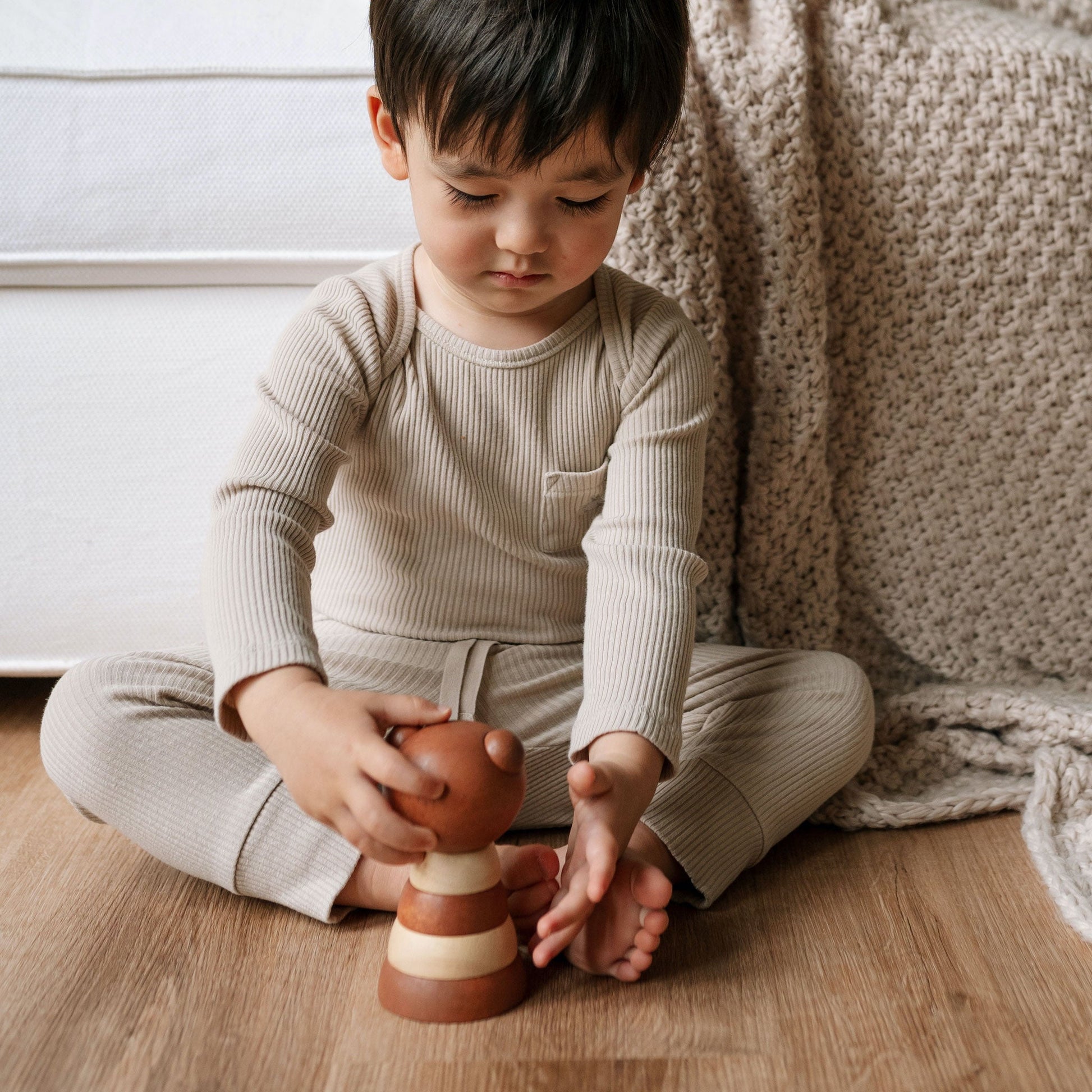Child playing with a wooden toy on a wooden floor.