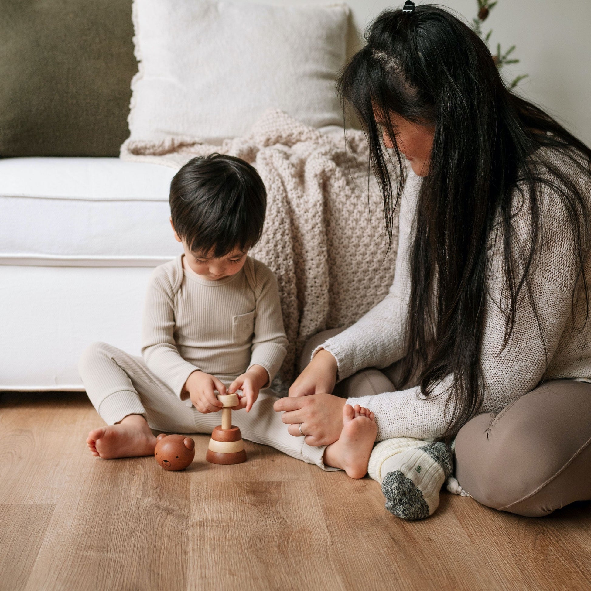 Woman and child playing with wooden toys on a wooden floor.