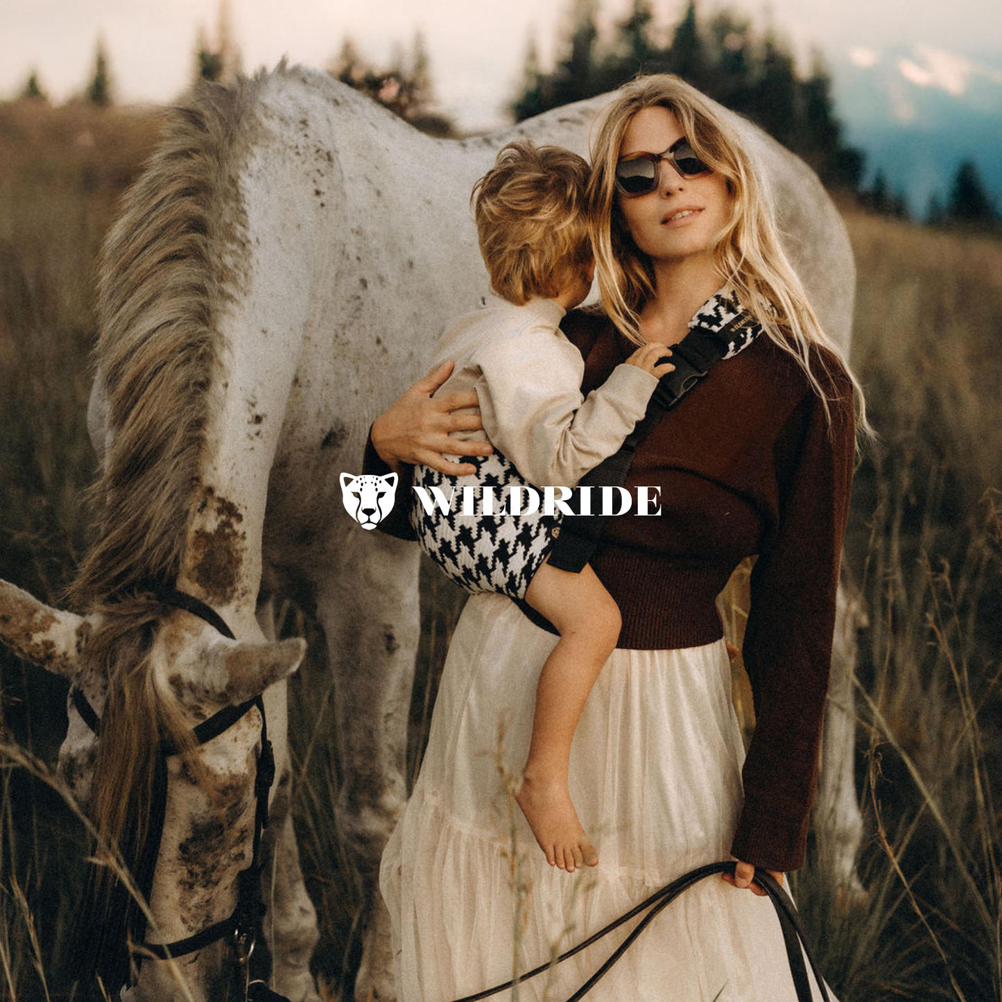 Woman holding a child next to a horse in a field with 'WildRide' branding.