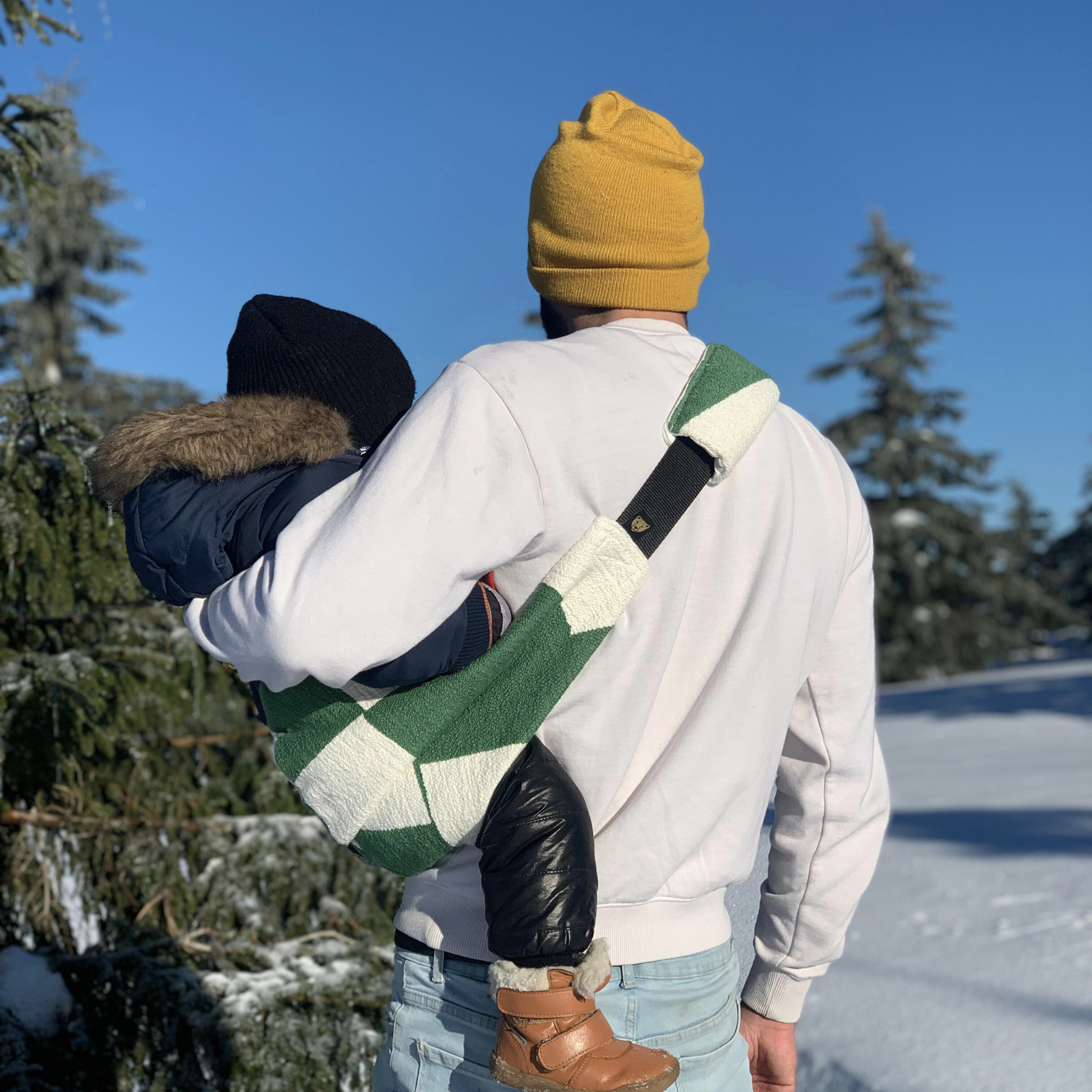 Two people walking in a snowy landscape with trees and clear blue sky.