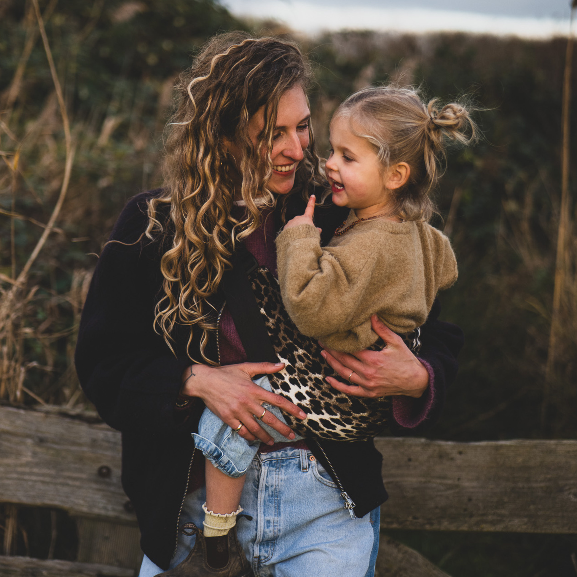Woman holding a young child in an outdoor setting with a wooden fence and natural background.