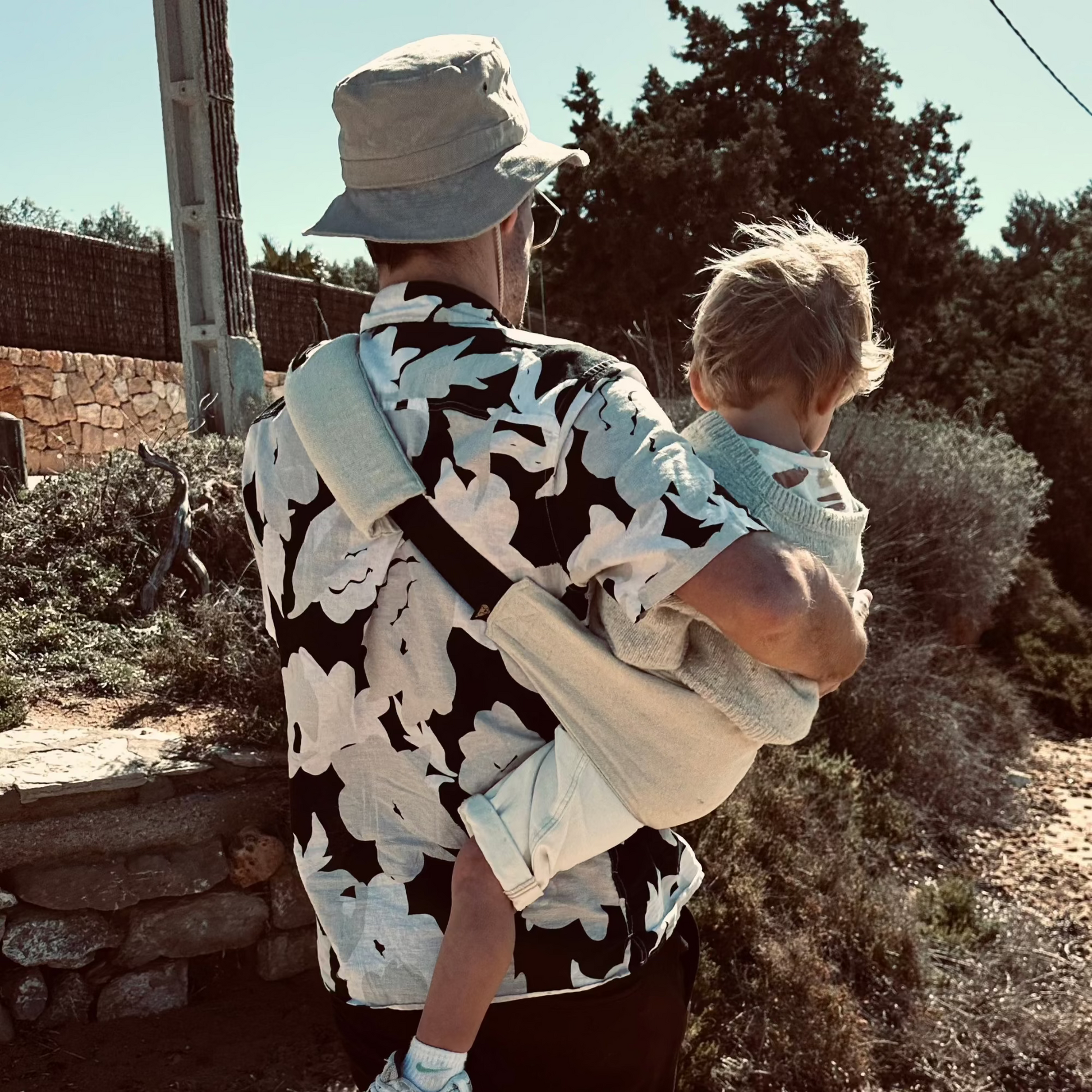 Person carrying a child on their back outdoors with trees and rocks in the background