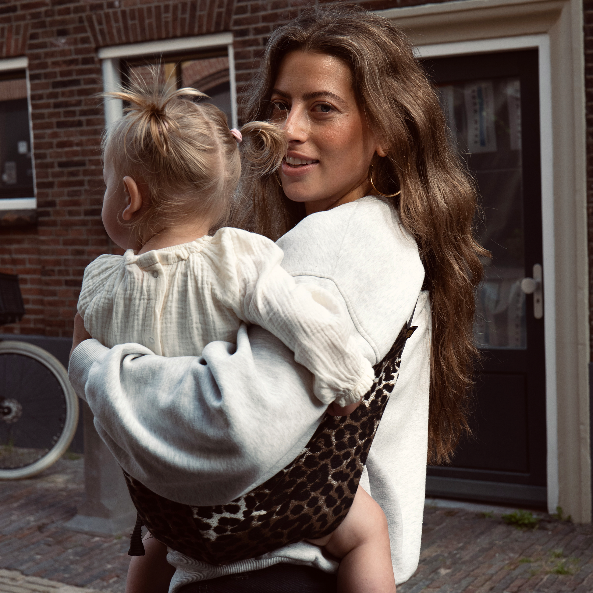 Woman carrying a child in a leopard print baby carrier outdoors.