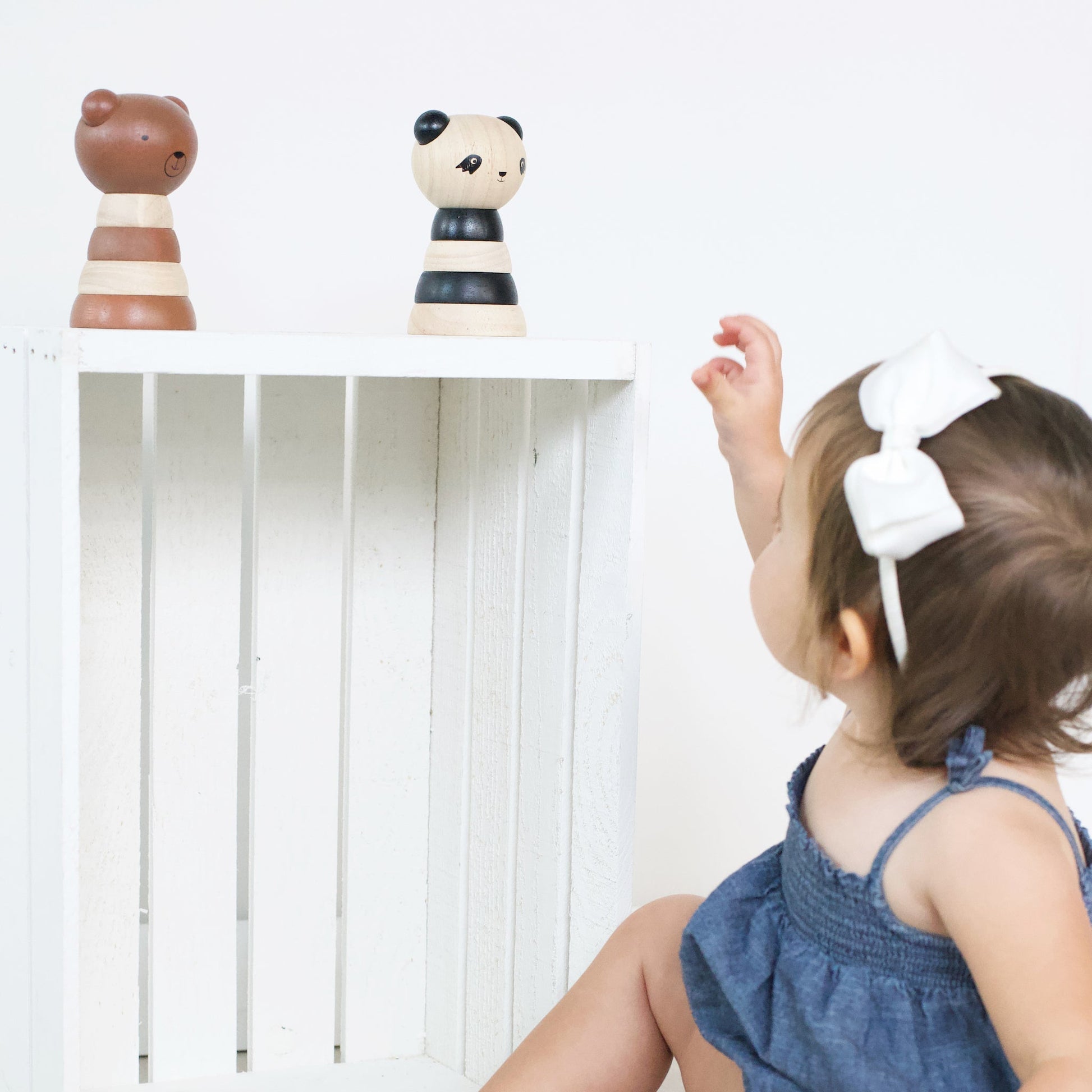 Child reaching towards wooden toys on a shelf with a white background