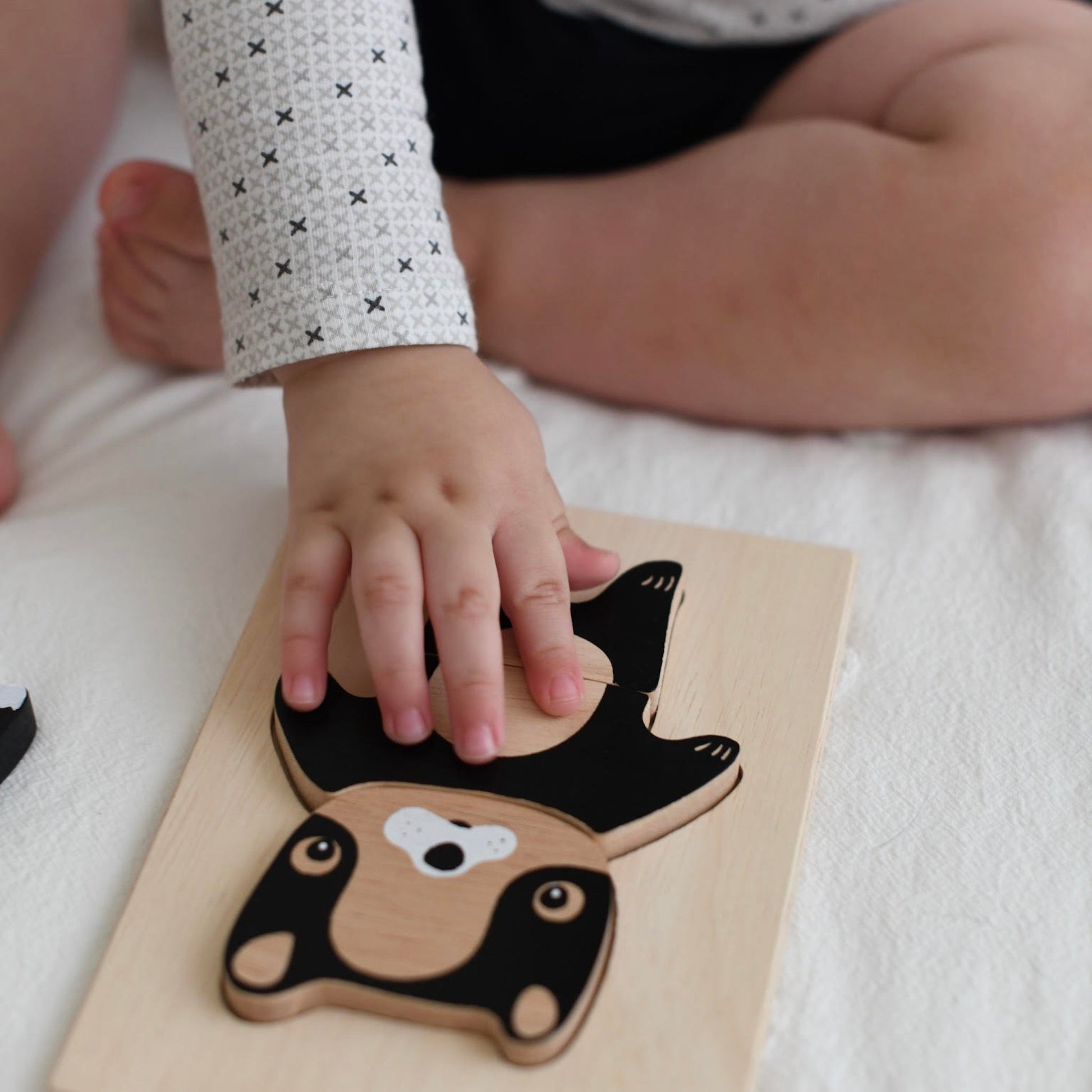 Child's hand interacting with a wooden animal puzzle on a white surface