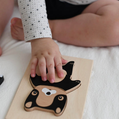 Child's hand interacting with a wooden animal puzzle on a white surface