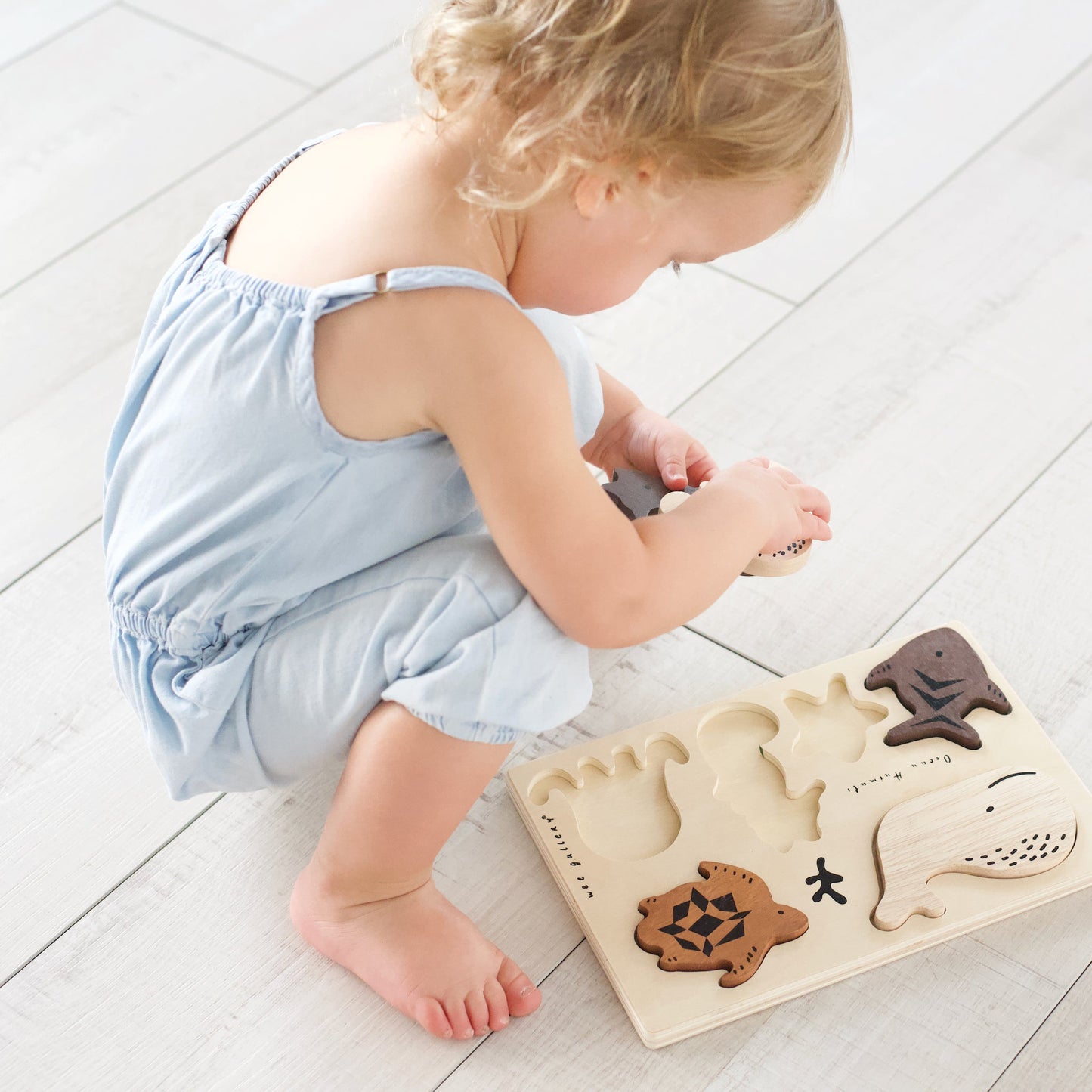 Child playing with a wooden puzzle on a light wooden floor
