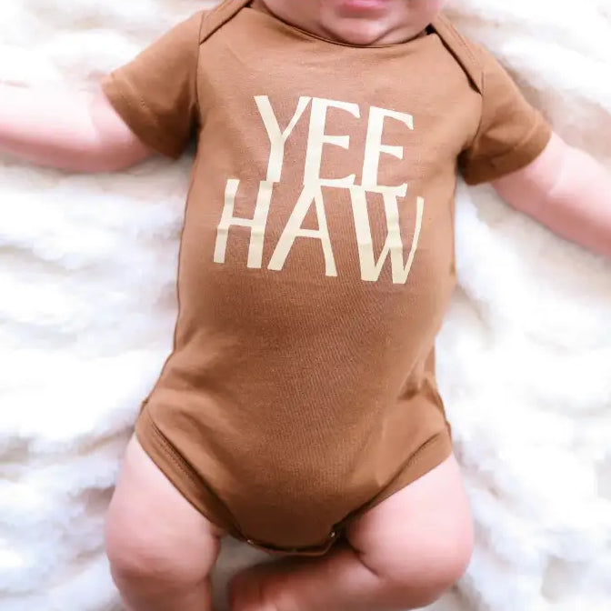 Baby wearing a brown onesie with 'YEE HAW' text on a white fluffy blanket